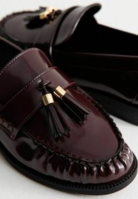 Mocassini in pelle verniciata bordeaux con dettagli a nappina e hardware dorato. Presentano dettagli cuciti e una punta arrotondata.