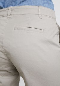 Pantalon en coton beige à coupe classique, doté d'une poche arrière et d'une texture subtile. Conçu pour un usage décontracté.