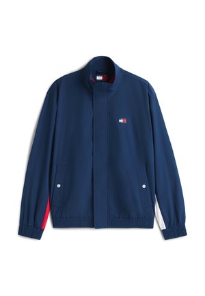 Casual jakna mornarsko modre barve s stoječim ovratnikom, elastičnimi manšetami in robom, sprednjimi žepi na prijem ter majhno rdeče-belo-modro logotipom na prsnem delu.