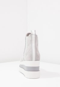 Harmaat mokkasaappaat nilkkapituisilla, joissa on tekstuuri pintakuvio, joustavat sivupaneelit ja pinottu valkoinen pohja, jossa on harmaa raitatavoite pohjassa.