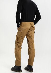 Cargo-byxor i beige, med flera sidofickor, en smal passform och en mjuk tygtextur. Bärs med en svart långärmad topp och svarta stövlar.