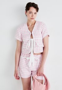 Rosa og hvit rutete kortermet topp med knytedetalj foran, matchende shorts og en rosa veske. Strukturert stoff med slitte kanter.