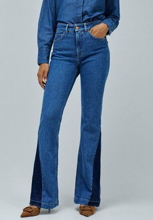 Jeans de mezclilla acampanados en azul medio con paneles laterales de un azul oscuro en contraste. Cuenta con cinco bolsillos, una cintura alta y un cierre de botón.