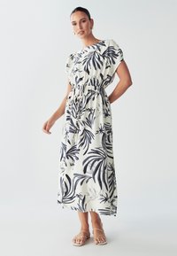 Maxi obleka iz lahkega materiala, z belo podlago in mornarsko modrim tropskim listnatim vzorcem, z elastiko v pasu in kratkimi rokavi. Uporabljene so preproste sandale.