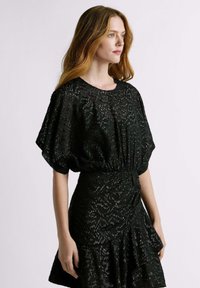 Robe noire avec motif texturé, manches courtes bouffantes, taille cintrée et ourlet à volants en couches. Le tissu a une finition brillante.