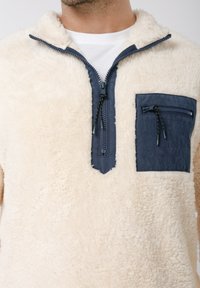 Φούτερ από φλις σε εκρού χρώμα με τσέπη στο στήθος με φερμουάρ σε ναυτικό μπλε. Διαθέτει γιακά με μισό φερμουάρ και υφή απαλή και αφράτ η.