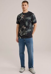 Fél hosszú ujjú fekete póló, trópusi levélmintával; világoskék farmernadrággal és szürke slip-on cipőkkel párosítva.