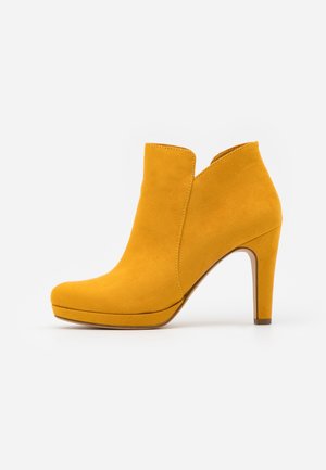 Gelbe Wildleder-Ankle-Boots mit einem geschwungenen Ausschnitt-Design, spitzer Zehenform und hohen Absatz. Glatte Textur mit einer Plateau-Sohle für zusätzlichen Auftrieb.
