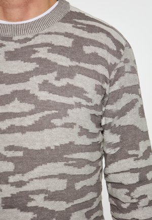 Pulover tricotat cu un model de camuflaj gri și bej, având un decolteu rotund și manșete cu nervuri, cu un finisaj texturat al țesăturii.