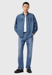 Koszula dżinsowa z dwoma kieszeniami na piersi, jasnoniebieska, w luźnym kroju, w połączeniu z wytartymi jasnoniebieskimi dżinsami i czarnymi butami.