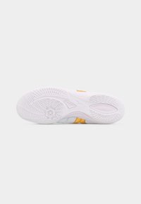 Σόλα λευκού αθλητικού παπουτσιού με κίτρινη ρίγα και υφή πέλματος σε ανοιχτό γκρι φόντο.