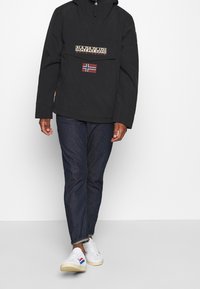 Zwarte hoodie met een voorzak, voorzien van logo-graphics en een Noorse vlagpatch. Gemaakt met donkere jeans en witte sneakers.