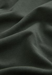 Tejido texturizado de color verde oscuro, drapeado con pliegues visibles, que muestra un fino patrón tejido y un acabado suave. Material ligero y versátil.