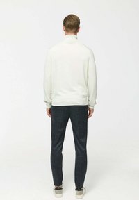 Pulover alb cu mânecă lungă și guler înalt, asortat cu pantaloni tapered gri închis și adidași ușori. Textură netedă și croială casual.