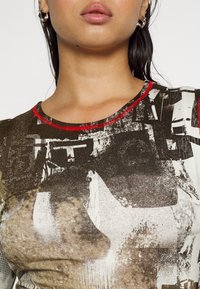 Grafisch t-shirt met een gestructureerd bruin-zwart patroon, een ronde halslijn en contrasterende rode biezen. Ontworpen voor een aansluitende pasvorm.