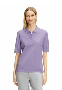 Lila Poloshirt mit kurzen Ärmeln, Kragen und einer Knopfleiste mit drei Knöpfen, aus einem glatten Stoff, kombiniert mit hellgrauen Hosen.