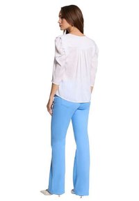 Camicia bianca con maniche a sbuffo e pieghe posteriori abbinata a pantaloni a campana blu chiaro. Le scarpe hanno la punta affusolata in una tonalità neutra.