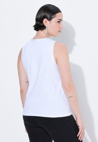 Top bianco senza maniche realizzato in tessuto morbido e leggero, con collo rotondo e silhouette aderente, abbinato a jeans scuri.