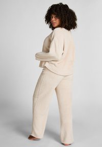 Beige, nep-bont lounge set met een losvallende, lange mouw top en rechte broekspijpen. Zachte textuur, minimale naden en een ontspannen ontwerp.