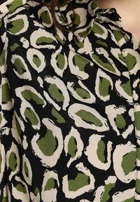 Tessuto nero con una bold stampa astratta di leopardo in beige e verde, caratterizzato da forme irregolari e una texture liscia.