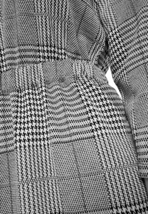 Tejido de patrón en blanco y negro que presenta diseños de pata de gallo y cuadros, con una superficie texturizada y una cinturilla elástica.