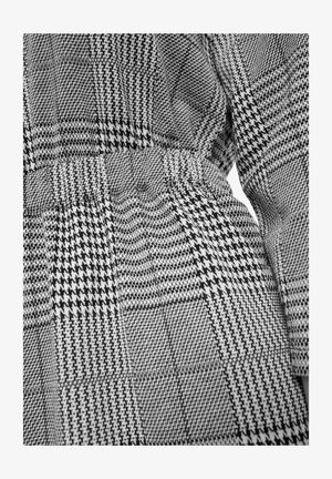 Czarnobiała tkanina w wzory o splocie houndstooth i kratę, z teksturowaną powierzchnią i elastycznym paskiem w talii.
