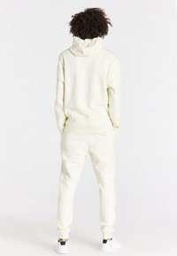 Krämfärgad hoodie med bakhuva, parat med matchande joggers. Slät, mjuk tygkvalitet med ribbade manschetter och minimalistiska detaljer.