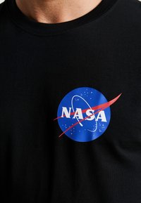 Black cotton t-shirt featuring a round NASA logo with a blue background, white letters, red swoosh, and white stars.