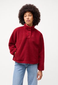 Rød, luksuriøs fleece-pullover med høy krage, fem-knappslukking, og sidelommer. Har en avslappet passform og strukturert overflate.