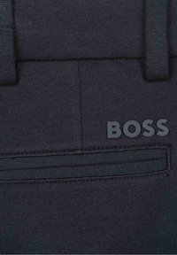 Tmavě námořnické kalhoty s hladkou texturou, vybavené zadní kapsou a hmatovým logem "BOSS" v šedé barvě. Elegantní design s přizpůsobeným střihem.