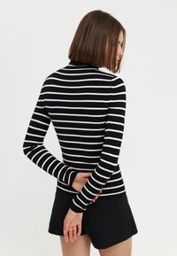 Črno-bela striped dolgosleeve majica s prilegajočim se dizajnom in rebrasto teksturo, v kombinaciji s črnimi kratkimi hlačami. Zadnji pogled prikazuje visok ovratnik.