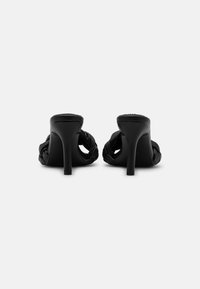 Sorte høye hæler med åpen bak, laget av flettet satengmateriale og med tynn stiletthæl. Glatt tekstur med en elegant finish.