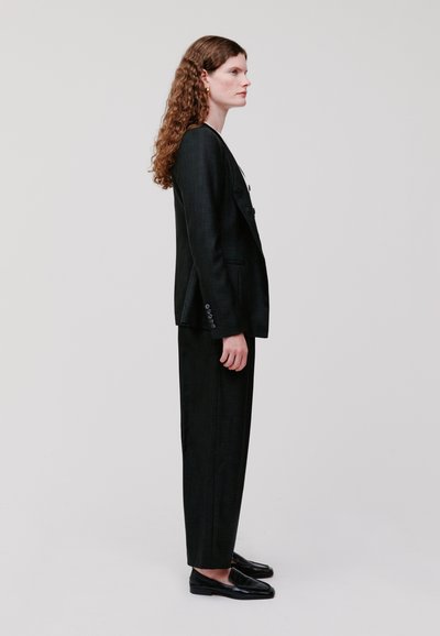 Completo sartorial nero caratterizzato da un blazer strutturato e pantaloni a vestibilità dritta. Tessuto liscio con una leggera trama, abbinato a scarpe basse.