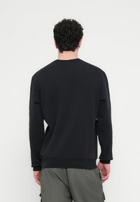 Felpa nera girocollo con maniche lunghe, realizzata in tessuto testurizzato. Caratterizzata da una vestibilità comoda e polsini a costine sull'orlo e sulle maniche.