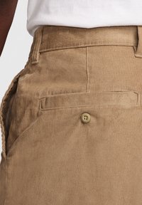 Beige kordflorsbyxor med en texturerad yta, med en sidoficka och en knapp för stängning på bakfickan.