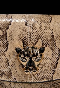 Käärmeennahkakuosiset beige clutch-laukku, joka on valmistettu keinonahasta. Laukussa on kultainen leopardipään lukko, joka on koristeltu mustilla ja kirkkailla kristalleilla.
