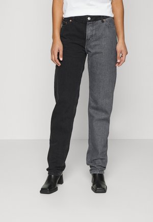 Person wearing two-tone jeans with one black and one gray leg, paired with black heeled boots and a white top.