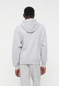 Sweat-shirt gris avec capuche à cordon, poignets et ourlet côtelés, présentant des éclaboussures de peinture au dos pour un look usé.