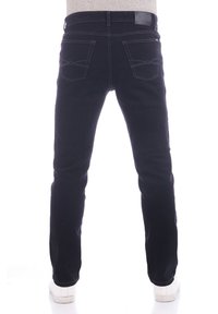 Jeans negros de corte ajustado, que cuentan con dos bolsillos traseros con costuras detalladas y una etiqueta de cuero en la cintura. Zapatillas blancas visibles.