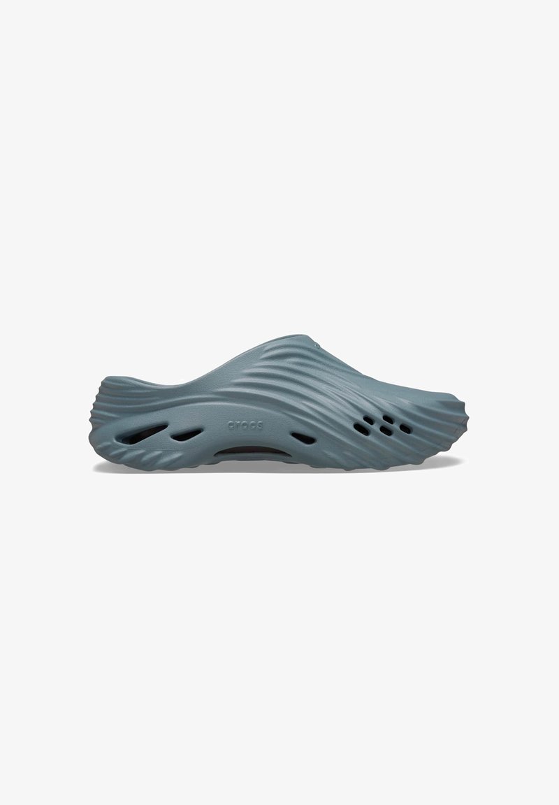 Light blue clog featuring a wavy design, made of durable material with ventilation holes along the sides. Smooth texture.
