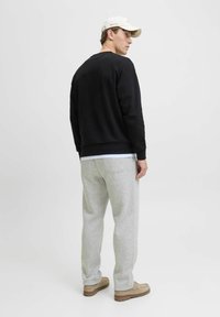 Zwarte sweatshirt met ronde hals, grijze trainingsbroek en beige schoenen. De outfit heeft een ontspannen pasvorm en een minimalistisch ontwerp.