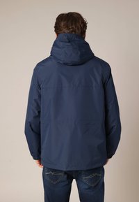 Veste légère bleu marine avec capuche, présentant une texture lisse et des poignets élastiques, conçue pour un usage casual. Vue de dos montrée.