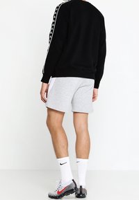 Svart sweatshirt med vita sidosträck, grå shorts, vita strumpor och gråsvart mönstrade sneakers, sedd bakifrån.