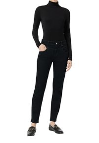 Zwarte coltrui gecombineerd met donkerblauwe jeans met voorzakken en een standaard knoopsluiting, aangevuld met zwarte instappers met hardwaredetails.