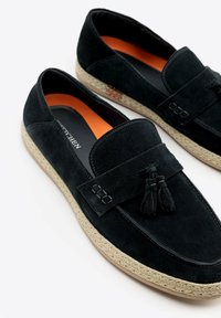 Černé semišové mokasíny s třásňovým páskem, v kontrastní oranžové podšívce a tkanou jutu podrážkou. Hladká textura a klasický design.