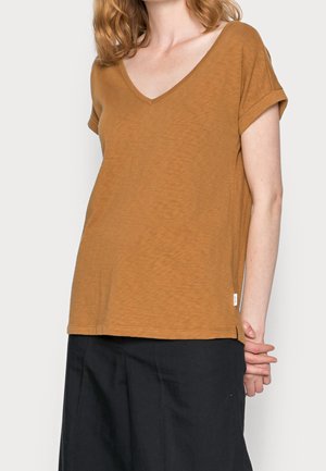 Brązowy t-shirt z krótkim rękawem i dekoltem w serek, wykonany z miękkiej tkaniny, z podwiniętymi rękawami i luźnym krojem, w zestawieniu z czarnymi spodniami.