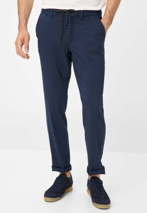 Marineblaue Hose mit lockerer Passform, elastischem Bund und Kordelzug. Mit Seitentaschen und hochgekrempelten Säumen. Kombiniert mit dunklen Sneakers.