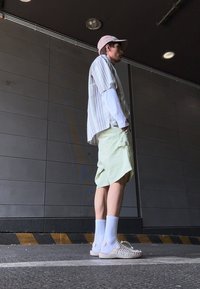 O ținută casual care include o cămașă cu mânecă scurtă în dungi, pantaloni scurți verzi lime cu textură, șosete albe până la genunchi și pantofi împletiți.