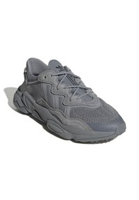 Sneakers sportivi grigi con un mix di materiali in rete e suede, dotati di un design con lacci, superiore testurizzato e una suola in gomma spessa.