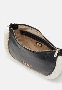 Pochette nera in ecopelle con rifiniture in ecopelliccia crema. Chiusura con zip dorata e tasca interna. Foderata con un motivo beige che presenta il marchio "GUESS."
